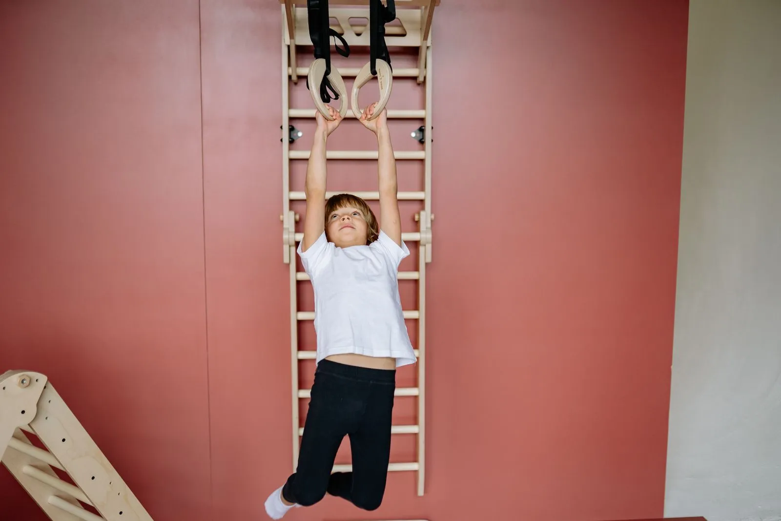 Young boy having fun and building strength on indoor gym rings at home.